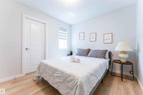 Light-filled room featuring wood-finish flooring, a white two-panel door, and a horizontal window with blinds - 8426 228A Street Nw, Edmonton, AB - Indoor Photo Showing Bedroom