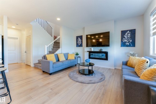 Bright living area featuring light wood-finish flooring, recessed lighting, a modern wall-mounted electric fireplace, and a light-filtering window treatment - 8426 228A Street Nw, Edmonton, AB - Indoor Photo Showing Living Room