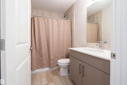 Bathroom featuring a modern vanity with integrated sink, chrome faucet, a mirrored wall, and a shower with light-toned wall tiling - 8426 228A Street Nw, Edmonton, AB - Indoor Photo Showing Bathroom
