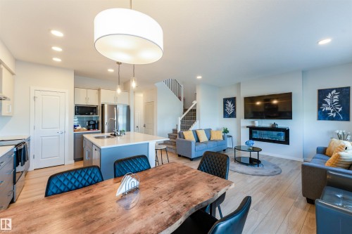 Open-concept living space featuring wood-finish flooring, a contemporary kitchen island with seating, stainless steel appliances, and a wall-mounted electric fireplace - 8426 228A Street Nw, Edmonton, AB - Indoor