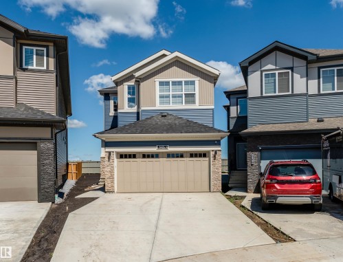 Contemporary two-story exterior featuring a two-tone blue and beige siding, stone accents, a dual-bay garage, concrete driveway, and white-trimmed windows - 8426 228A Street Nw, Edmonton, AB - Outdoor With Facade