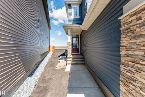 Front entrance featuring stone facade accents, dark blue horizontal siding, and a deep red entry door with an upper glass panel - 8426 228A Street Nw, Edmonton, AB -  With Exterior