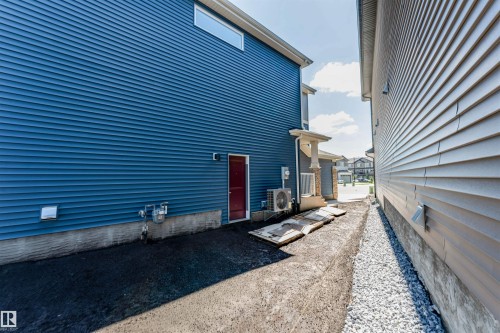 Blue horizontal vinyl siding exterior with a red entry door, a compact air conditioning unit, and a high-set horizontal window - 8426 228A Street Nw, Edmonton, AB - Outdoor With Exterior