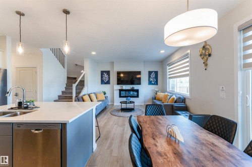 Open-concept living area featuring wood-finish flooring, a contemporary fireplace, and a kitchen island with a stainless steel sink and dishwasher - 8426 228A Street Nw, Edmonton, AB - Indoor