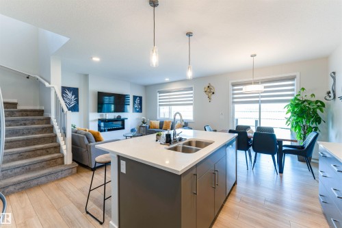 Open-concept living area featuring wood-finish flooring, a kitchen island with a double sink and white countertop, and a dining area with a modern chandelier - 8426 228A Street Nw, Edmonton, AB - Indoor Photo Showing Kitchen With Double Sink