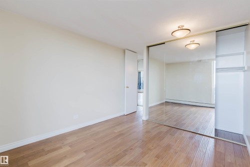 Room featuring wood-finish flooring, white baseboards, and a mirrored sliding closet door - 904 10883 Saskatchewan Drive, Edmonton, AB 