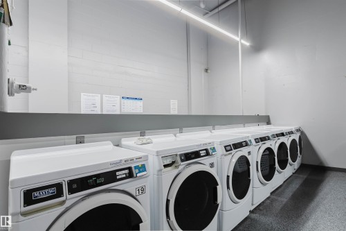 On-site laundry facility featuring multiple front-loading washers and dryers, white appliances, durable flooring, and ample overhead lighting - 904 10883 Saskatchewan Drive, Edmonton, AB 