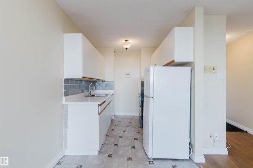 Galley kitchen featuring white cabinetry, light countertops, subway tile backsplash, and patterned tile flooring - 904 10883 Saskatchewan Drive, Edmonton, AB 