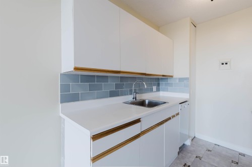 Kitchenette featuring white cabinetry with integrated wood-tone pulls, a subway tile backsplash, and a stainless steel sink with a gooseneck faucet - 904 10883 Saskatchewan Drive, Edmonton, AB 