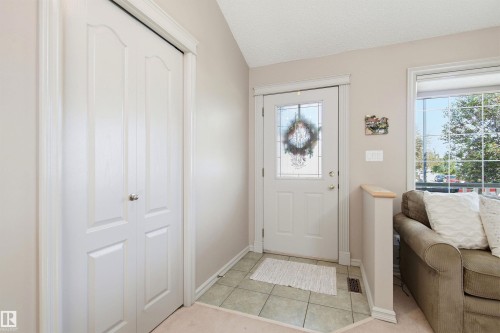 Entryway featuring a white paneled door with decorative glass inserts, bi-fold closet doors, square tile flooring, and a large window with white framing - 11715 11B Avenue, Edmonton, AB 