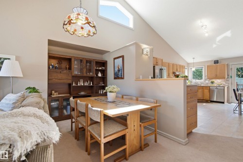 Open-concept dining area featuring a vaulted ceiling with a high transom window, built-in shelving, an ornamental stained-glass pendant light, and a pass-through to the kitchen with wood cabinetry - 11715 11B Avenue, Edmonton, AB 