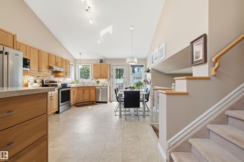 Open-concept kitchen and dining area featuring vaulted ceilings, wood-finish cabinetry, stainless steel appliances, and light-toned tile flooring - 11715 11B Avenue, Edmonton, AB 