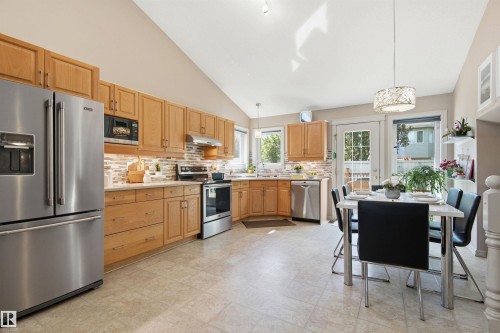Bright kitchen and dining area featuring light wood cabinetry, stainless steel appliances, and a tiled backsplash - 11715 11B Avenue, Edmonton, AB 