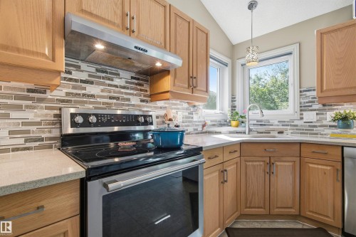 Light wood cabinetry with stainless steel appliances and a neutral mosaic tile backsplash - 11715 11B Avenue, Edmonton, AB 