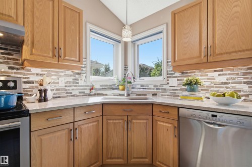 Kitchen featuring wood cabinetry, light-toned countertops, a mosaic tile backsplash, and stainless steel appliances - 11715 11B Avenue, Edmonton, AB 