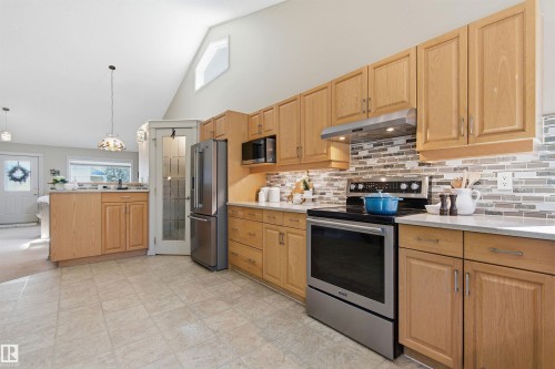 Kitchen featuring light wood cabinetry, a mosaic tile backsplash, stainless steel appliances, and a vaulted ceiling with a high triangular window - 11715 11B Avenue, Edmonton, AB 