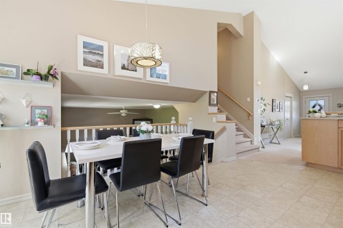 Vaulted ceilings enhance this open-concept dining area featuring tile flooring, a contemporary pendant light fixture, and a staircase with a white balustrade - 11715 11B Avenue, Edmonton, AB 