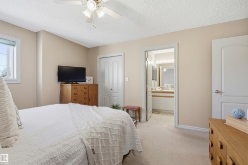 Carpeted bedroom featuring a ceiling fan with light fixture, a window with a blind, and a doorway leading to a bathroom with a double vanity - 11715 11B Avenue, Edmonton, AB 