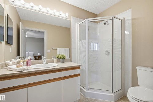 Bathroom featuring a corner shower with glass enclosure, single vanity with integrated sink, textured countertop, and full-width mirror with overhead bar lighting - 11715 11B Avenue, Edmonton, AB 