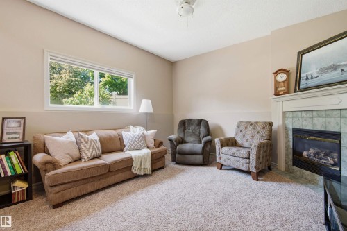 Living area featuring a double window, broadloom carpeting, a built-in fireplace with a tile surround and mantel, and painted walls - 11715 11B Avenue, Edmonton, AB 