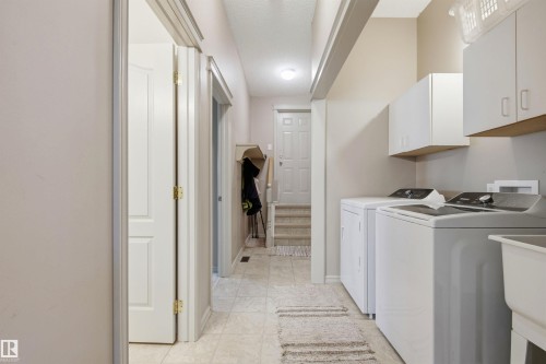 Dedicated laundry area featuring white upper cabinetry, a utility sink, and tiled flooring - 11715 11B Avenue, Edmonton, AB 
