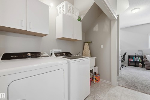 Dedicated laundry area featuring white upper cabinetry, a utility sink, and tiled flooring - 11715 11B Avenue, Edmonton, AB 