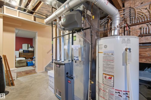 Basement utility area featuring a hot water heater and furnace with exposed ductwork - 11715 11B Avenue, Edmonton, AB 