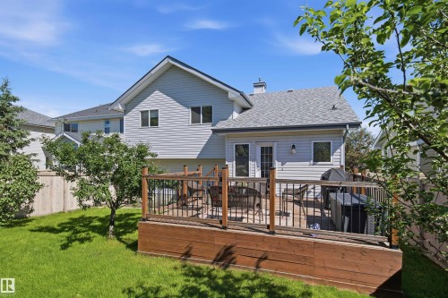 Rear exterior with light-colored siding, a tiered wood deck, and a manicured lawn - 11715 11B Avenue, Edmonton, AB 