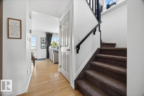 Entryway featuring wood-finish flooring, a white paneled door, and a staircase with carpeted treads and a black handrail - 3934 160 Avenue, Edmonton, AB 
