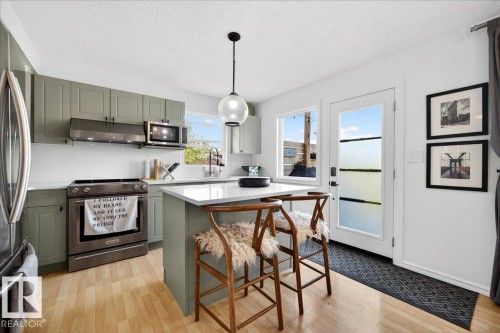 Modern kitchen featuring sage green cabinetry, stainless steel appliances, and wood-finish flooring - 3934 160 Avenue, Edmonton, AB 