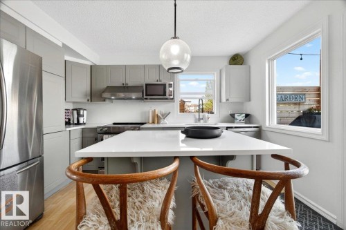 Kitchen featuring a large central island with seating, stainless steel appliances, light gray cabinetry, and white countertops - 3934 160 Avenue, Edmonton, AB 