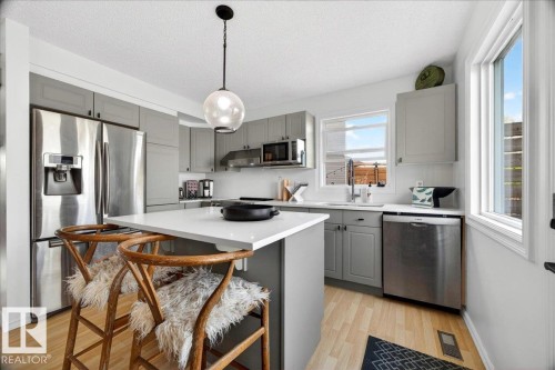 Kitchen featuring light gray cabinetry, stainless steel appliances, a white island countertop, and wood-finish flooring - 3934 160 Avenue, Edmonton, AB 