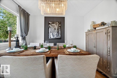Dining area featuring a contemporary chandelier, a built-in window with garden views, a substantial wood dining table, and upholstered dining chairs - 3934 160 Avenue, Edmonton, AB 