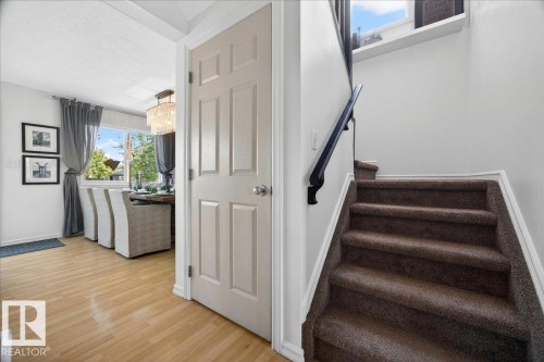 Interior entryway featuring wood-finish flooring, a six-panel door, and a carpeted staircase with a dark handrail - 3934 160 Avenue, Edmonton, AB 
