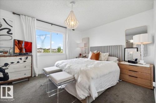 Spacious bedroom with carpeted flooring, a large window, and a decorative pendant light fixture - 3934 160 Avenue, Edmonton, AB 