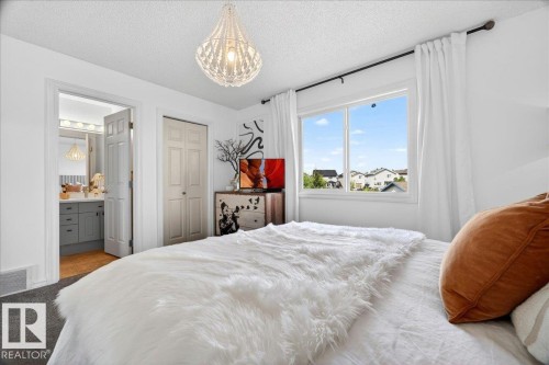 Bedroom featuring a window with white window treatments, a white beaded chandelier, and bi-fold closet doors - 3934 160 Avenue, Edmonton, AB 