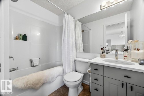 Bathroom featuring a white bathtub with a shower combination, a white toilet, and a vanity with a white countertop and gray cabinetry - 3934 160 Avenue, Edmonton, AB 