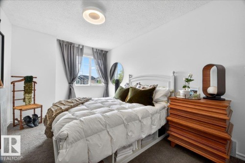 Carpeted bedroom featuring a window with gray drapes, a ceiling-mounted light fixture, a white bed frame, and a wood-finish dresser - 3934 160 Avenue, Edmonton, AB 