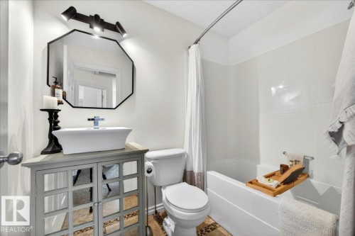 Bathroom featuring a vessel sink with chrome faucet, octagonal mirror, three-light track fixture, built-in bathtub with shower, and pebble-style floor tiling - 3934 160 Avenue, Edmonton, AB 