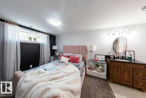 Bedroom featuring a window with sheer curtains, a plush headboard, and a built-in vanity with a dark countertop and wood-finish cabinetry - 3934 160 Avenue, Edmonton, AB 