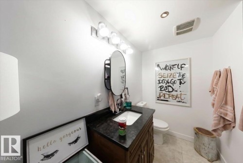 Bathroom featuring a wood vanity with a dark countertop and an oval mirror, illuminated by a multi-bulb vanity light fixture - 3934 160 Avenue, Edmonton, AB 