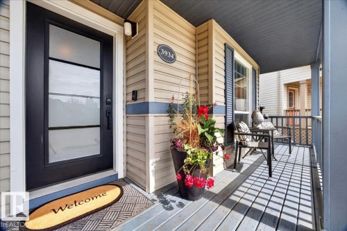 Covered front porch featuring light-colored siding with a blue accent band, a black paneled door with privacy glass inserts, and a black wall-mounted outdoor light fixture - 3934 160 Avenue, Edmonton, AB 