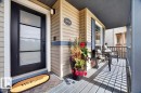 Covered front porch featuring light-colored siding with a blue accent band, a black paneled door with privacy glass inserts, and a black wall-mounted outdoor light fixture - 3934 160 Avenue, Edmonton, AB 