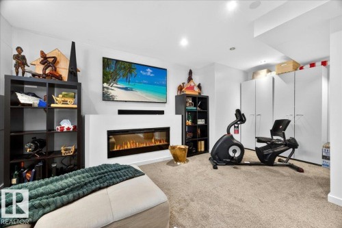 Recessed lighting illuminates a carpeted recreation room featuring a built-in linear fireplace with a television mounted above, and floor-to-ceiling cabinetry with white panels - 3934 160 Avenue, Edmonton, AB 
