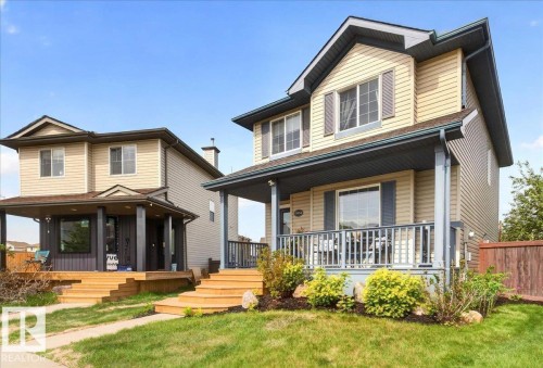 Two-story residence featuring light-colored siding, a covered front porch with dark grey railings, and a contrasting dark roofline - 3934 160 Avenue, Edmonton, AB 
