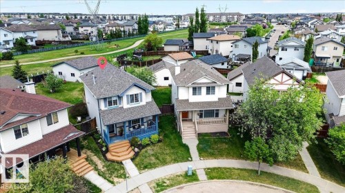 Two-story residence featuring a covered front porch with blue accents, dark shingle roofing, and a tiered wooden staircase at the entrance - 3934 160 Avenue, Edmonton, AB 