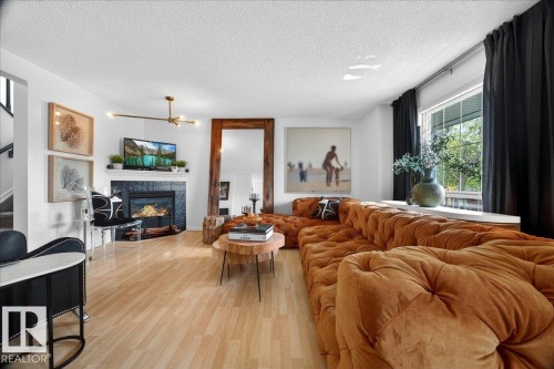 Living area with light wood-finish flooring, a fireplace featuring a dark tile surround and white mantel, and a large window - 3934 160 Avenue, Edmonton, AB 