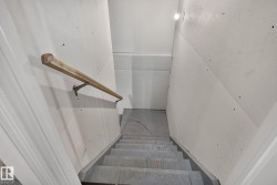 Staircase with a light wood handrail, white wall paneling, and a recessed ceiling light fixture - 