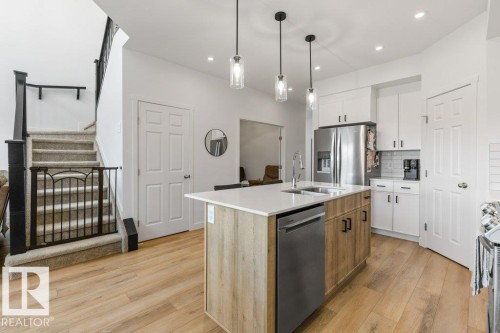 Modern kitchen featuring a central island with a built-in sink and stainless steel dishwasher - 25 Nettle Crescent, St. Albert, AB 