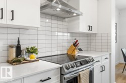 Contemporary kitchen featuring white cabinetry, quartz countertops, a tile backsplash, and a stainless steel range hood - 